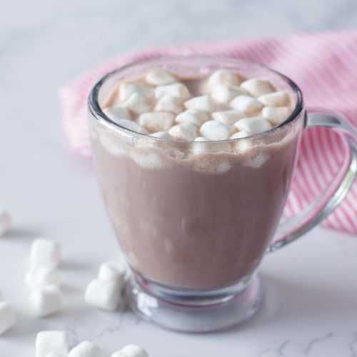Hot chocolate in a glass topped with mini marshmallows with white marshmallows on side