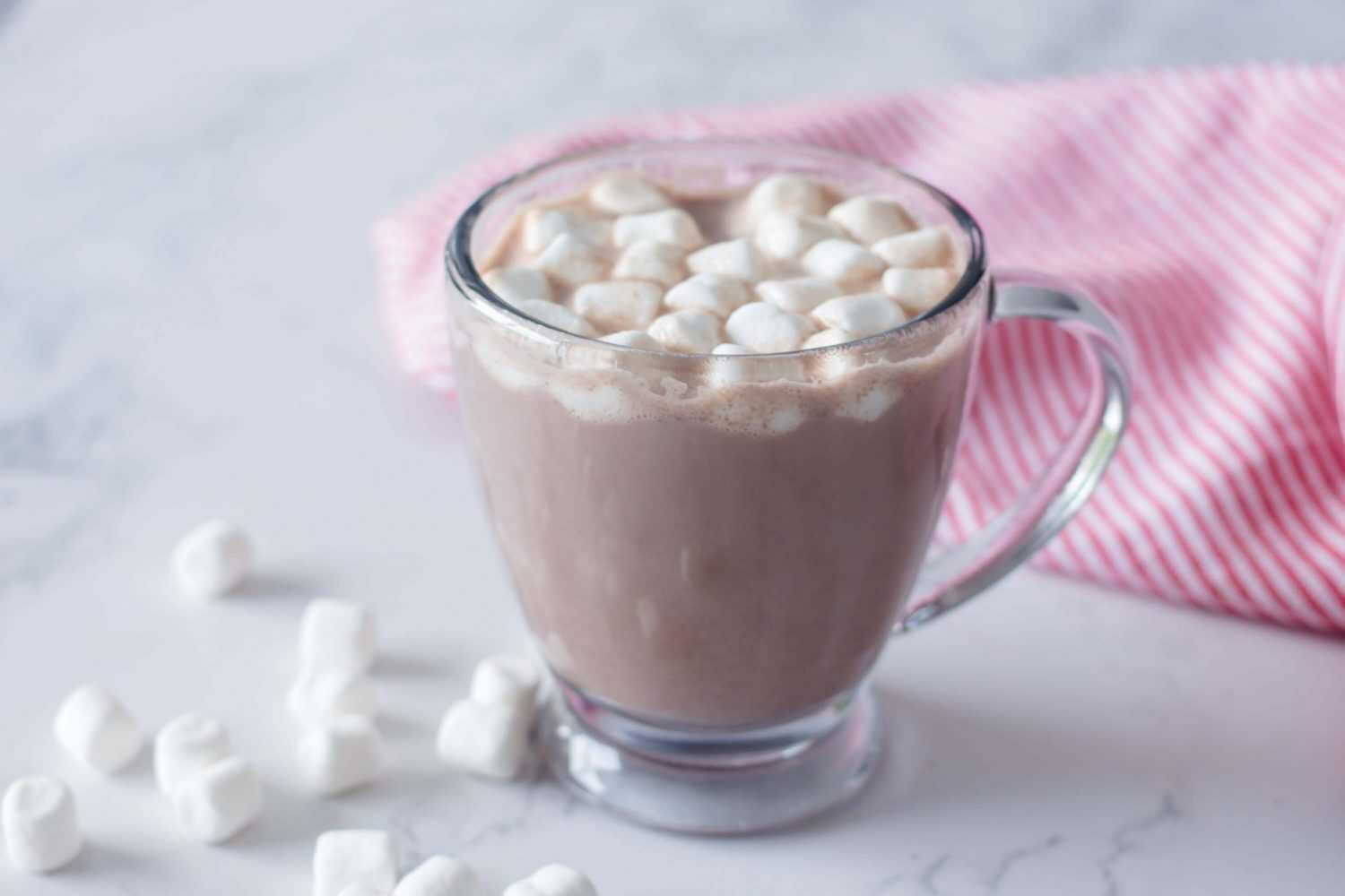 Hot chocolate in a glass topped with mini marshmallows with white marshmallows on side