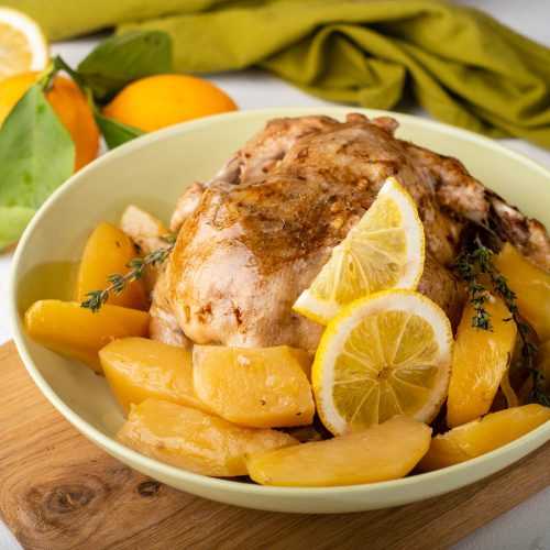 Whole chicken roasted served with potato slices and lemon slices in a white bowl