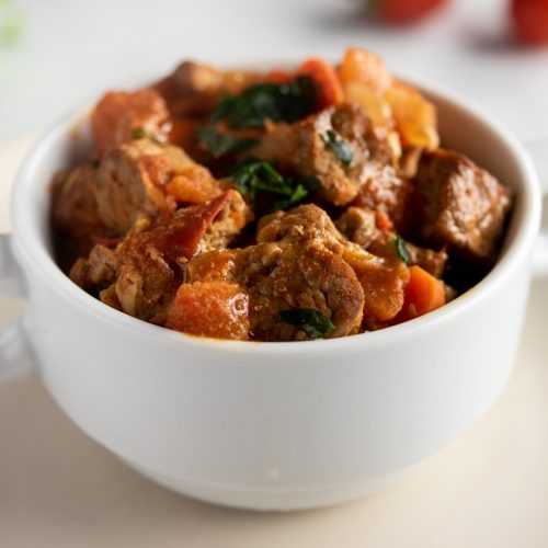 beef chunks with carrot cubes and potato cubes with parsley in a white bowl