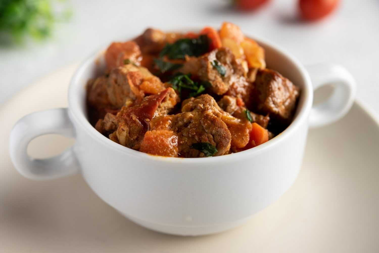 beef chunks with carrot cubes and potato cubes with parsley in a white bowl
