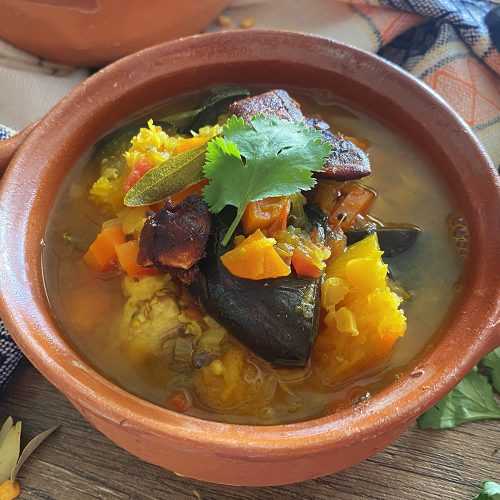 green soup with carrot cubes, pumpkin and eggplant cubes with parsley leaves on top in brown bowl