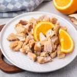 Roasted pork cubes with orange slices on side in white plate