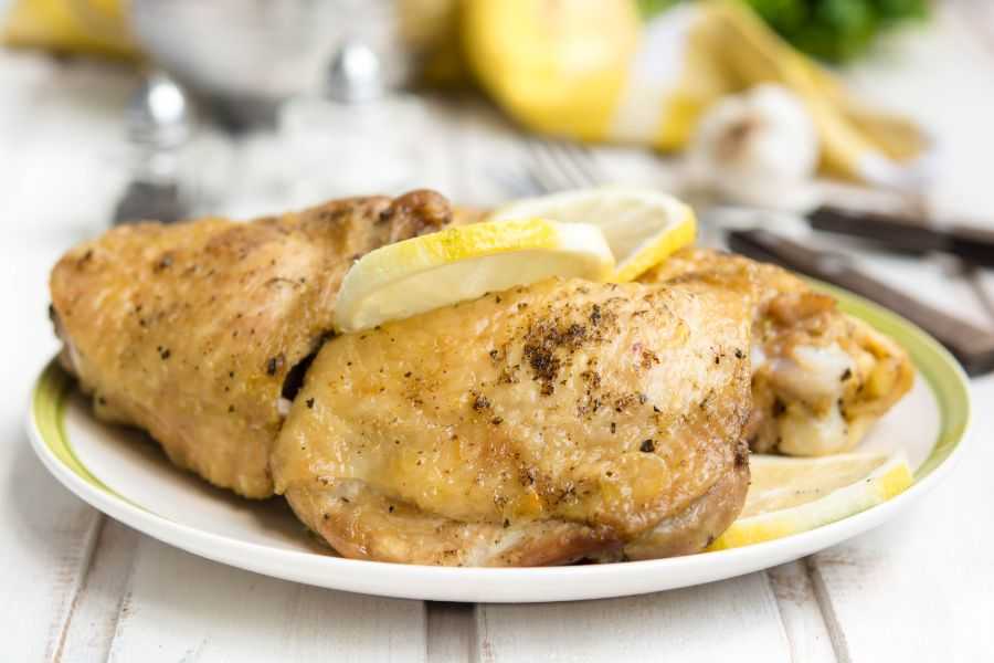 Chicken thighs with crispy skin topped with spices and lemon slices on a white plate