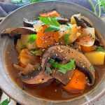 Sliced Portobello mushrooms mixed with chopped carrot and potatoes and parsley topped with spices in red soup