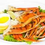 cooked crab legs on a plate with fresh parsley, lemon juice and lime slice