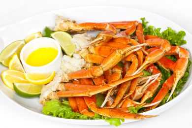 cooked crab legs on a plate with fresh parsley, lemon juice and lime slice