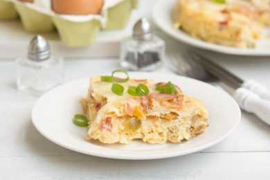 Baked egg casserole filled with bacon and vegetables topped with chopped scallion and melted cheese