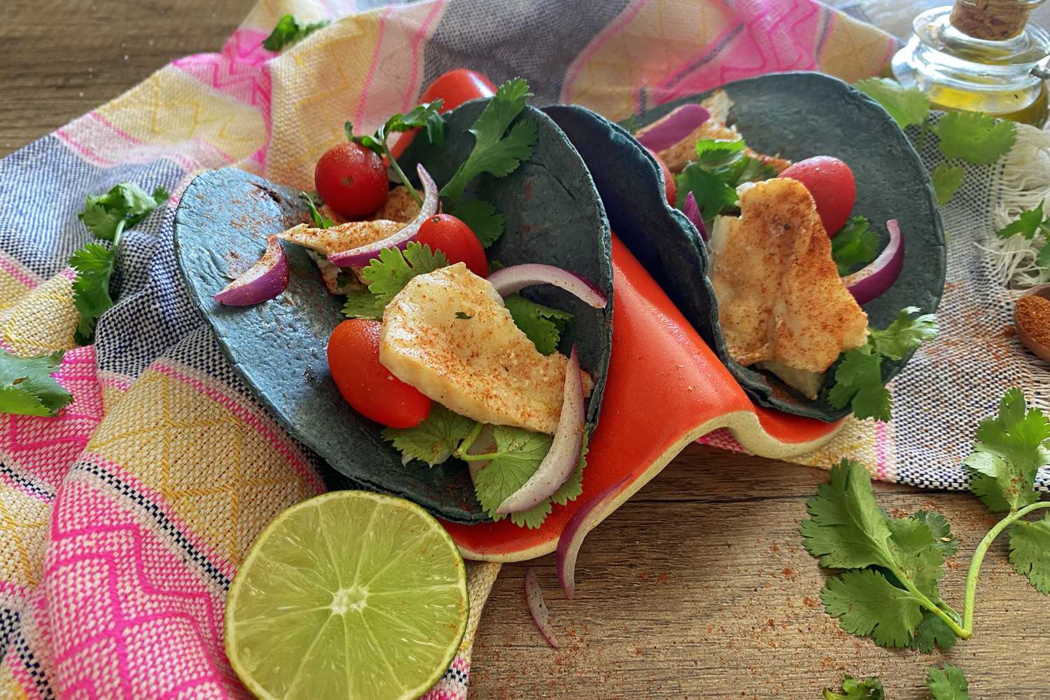 Two open tacos filled with fish pieces, cherry tomatoes, lettuce and red onion slices