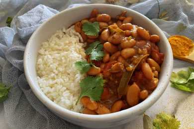 White rice with white beans in red sauce and fresh parsley on top on white bowl