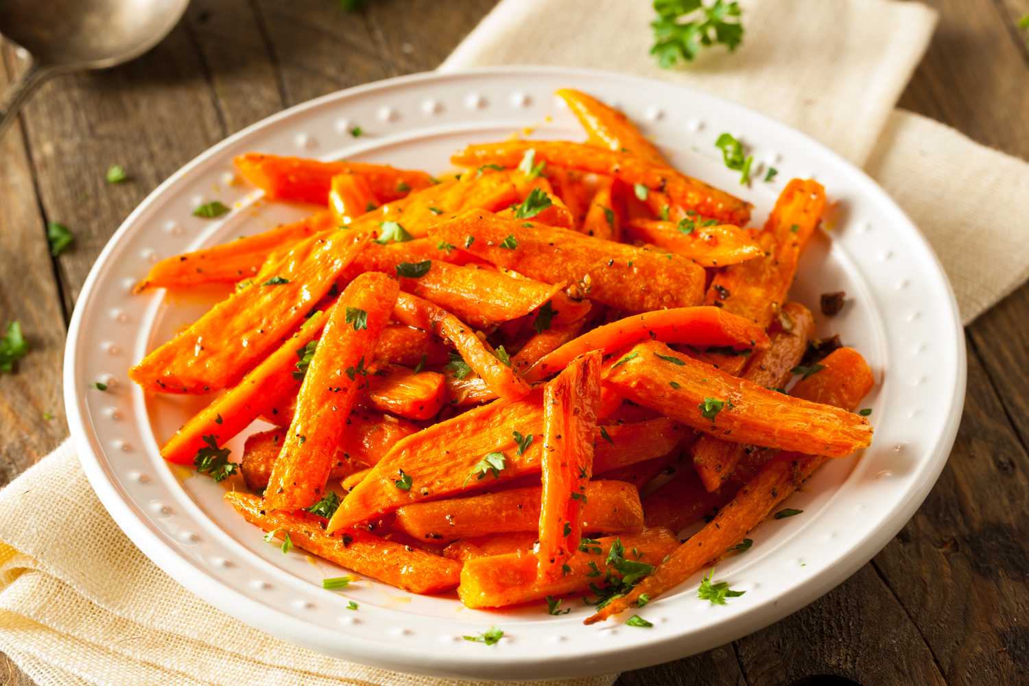 Carrot fries with spices and chopped parsley on top in white bowl