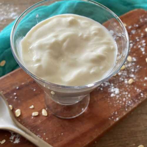 Griechischer Joghurt in Glasschüssel auf Schneidebrett mit Löffel an der Seite
