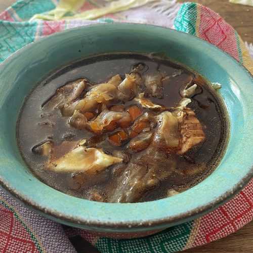 Brown soup filled with pork chunks, chopped cabbage and spices