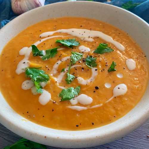 Pumpkin soup topped with sour cream, parsley and ground black pepper in white bowl