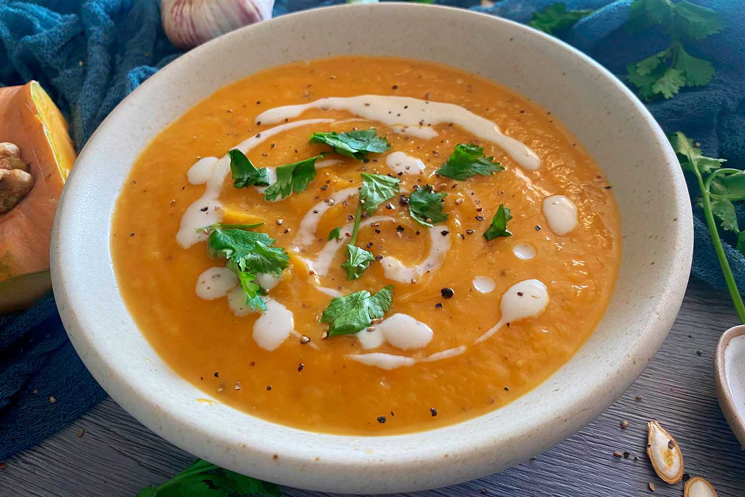 Pumpkin soup topped with sour cream, parsley and ground black pepper in white bowl
