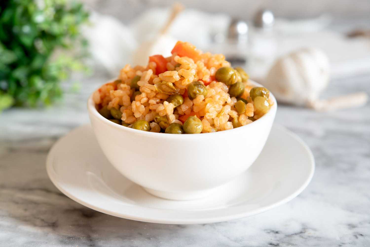 Rice mixed with peas, carrot cubes and spices in white bowl
