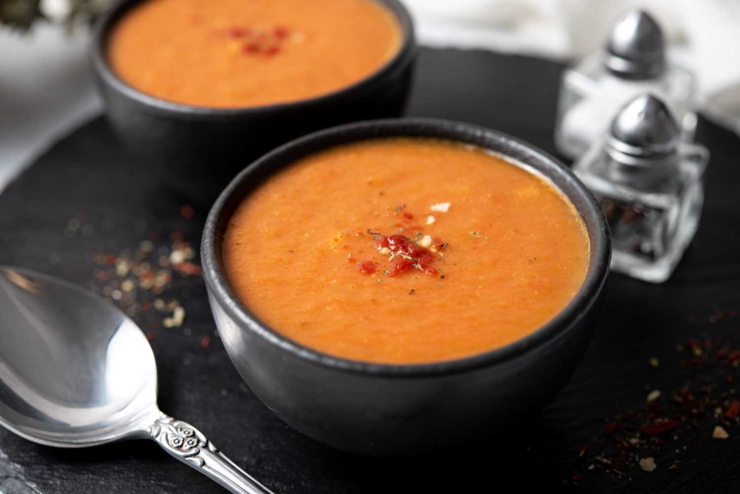 Blended tomato soup in two bowls topped with spices
