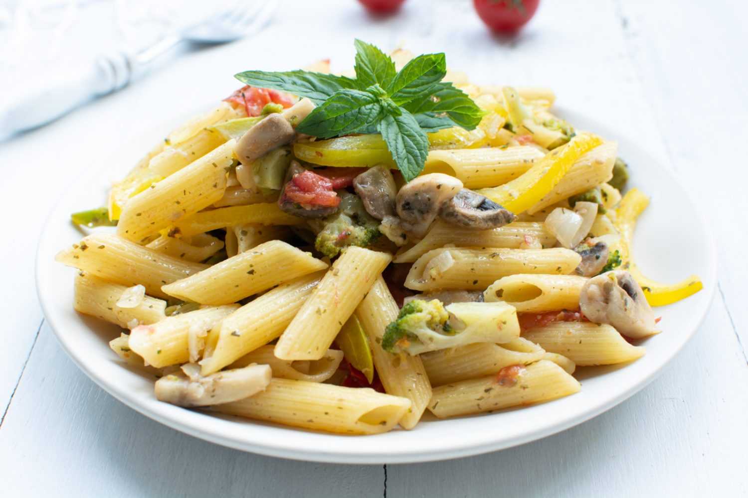 Penna pasta with tomatoes, mushrooms, spices and basil on top in white plate 