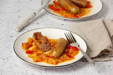 Sausage cut into half over roasted bell pepper strips with fork on white plate