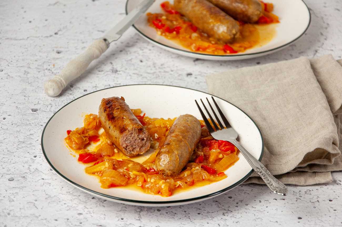 Sweet Italian sausage cut in half over roasted bell pepper strips with fork on white plate
