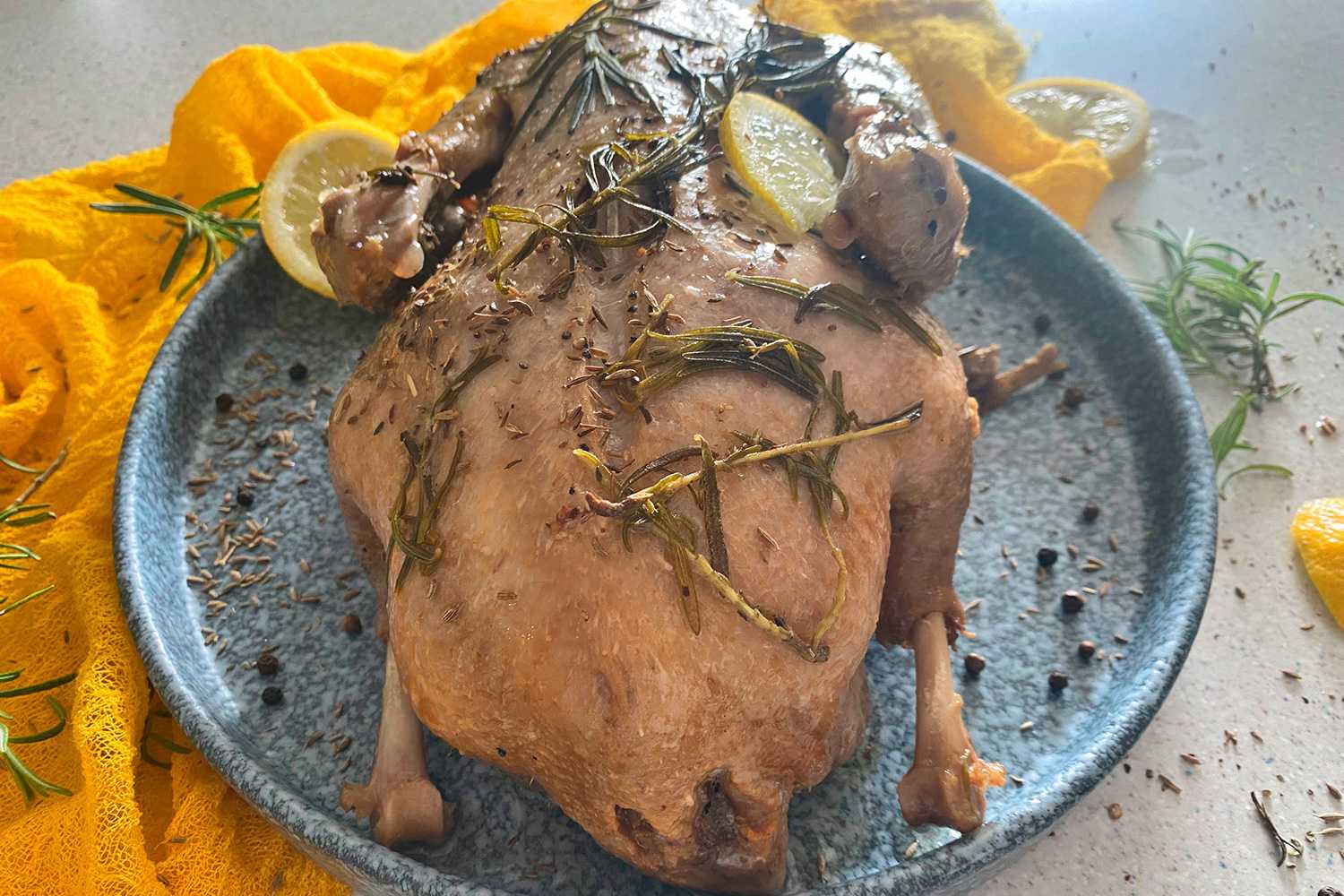 Whole duck roasted with rosemary, spices and lemon slices on top in blue plate