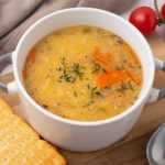 Yellow split pea soup filled with carrot cubes and spices with cracker on side