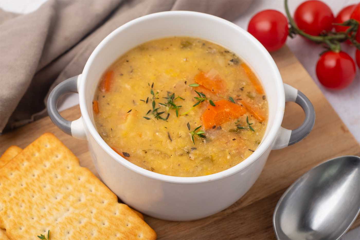 Yellow split pea soup filled with carrot cubes and spices with crackers on side