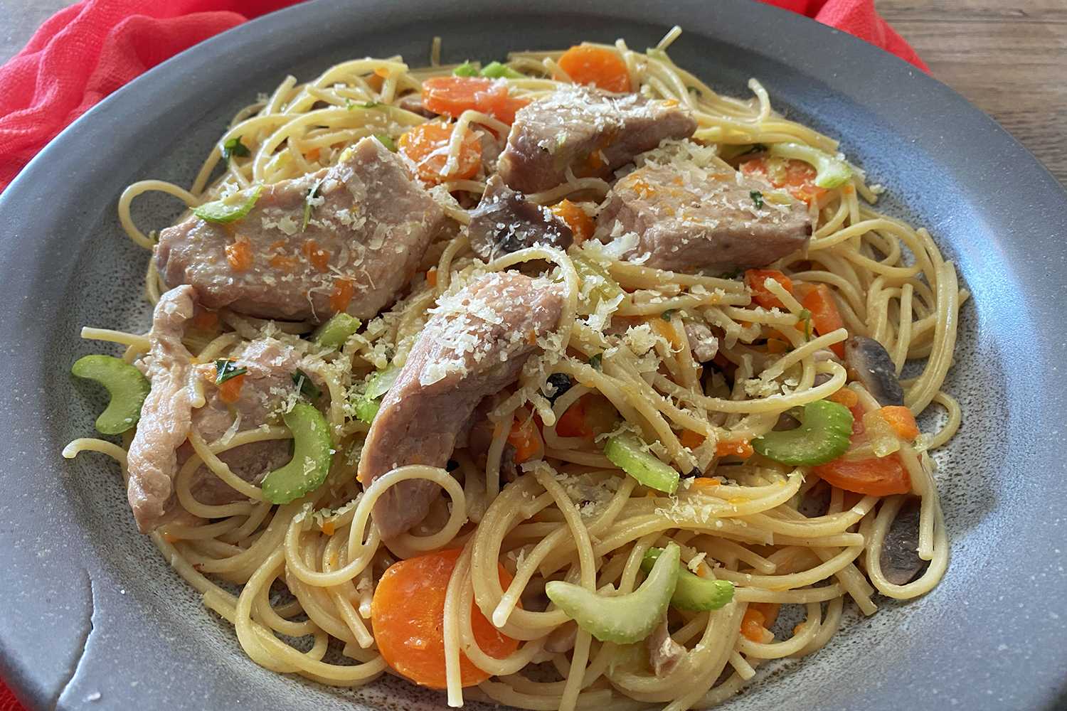 Egg noodles with beef chunks, carrot slices and celery slices on a blue plate