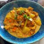 chicken cubes in a yellow curry sauce mixed with carrot and potato cubes with parsley on top