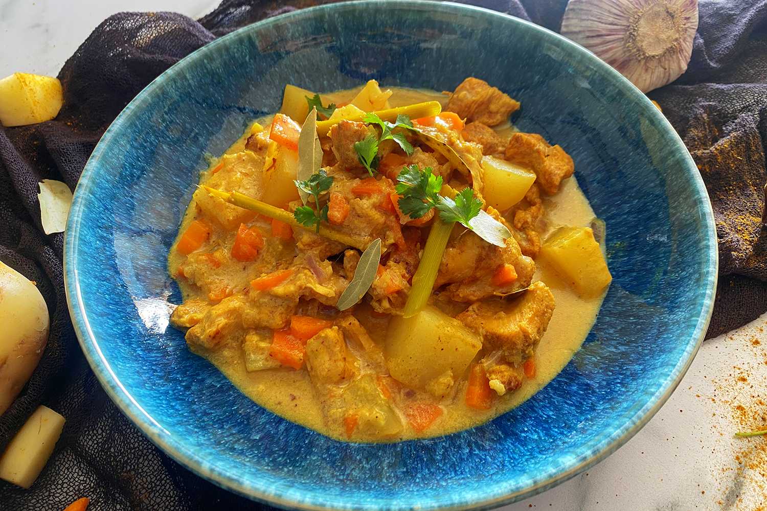 chicken cubes in a yellow curry sauce mixed with carrot and potato cubes with parsley on top