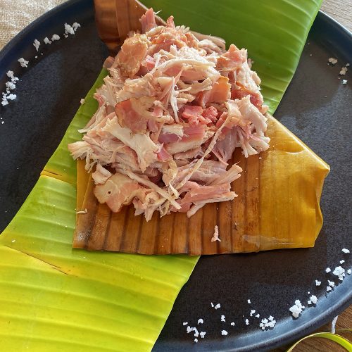 Kalua Pork mixed with bacon on banana leaf on black plate