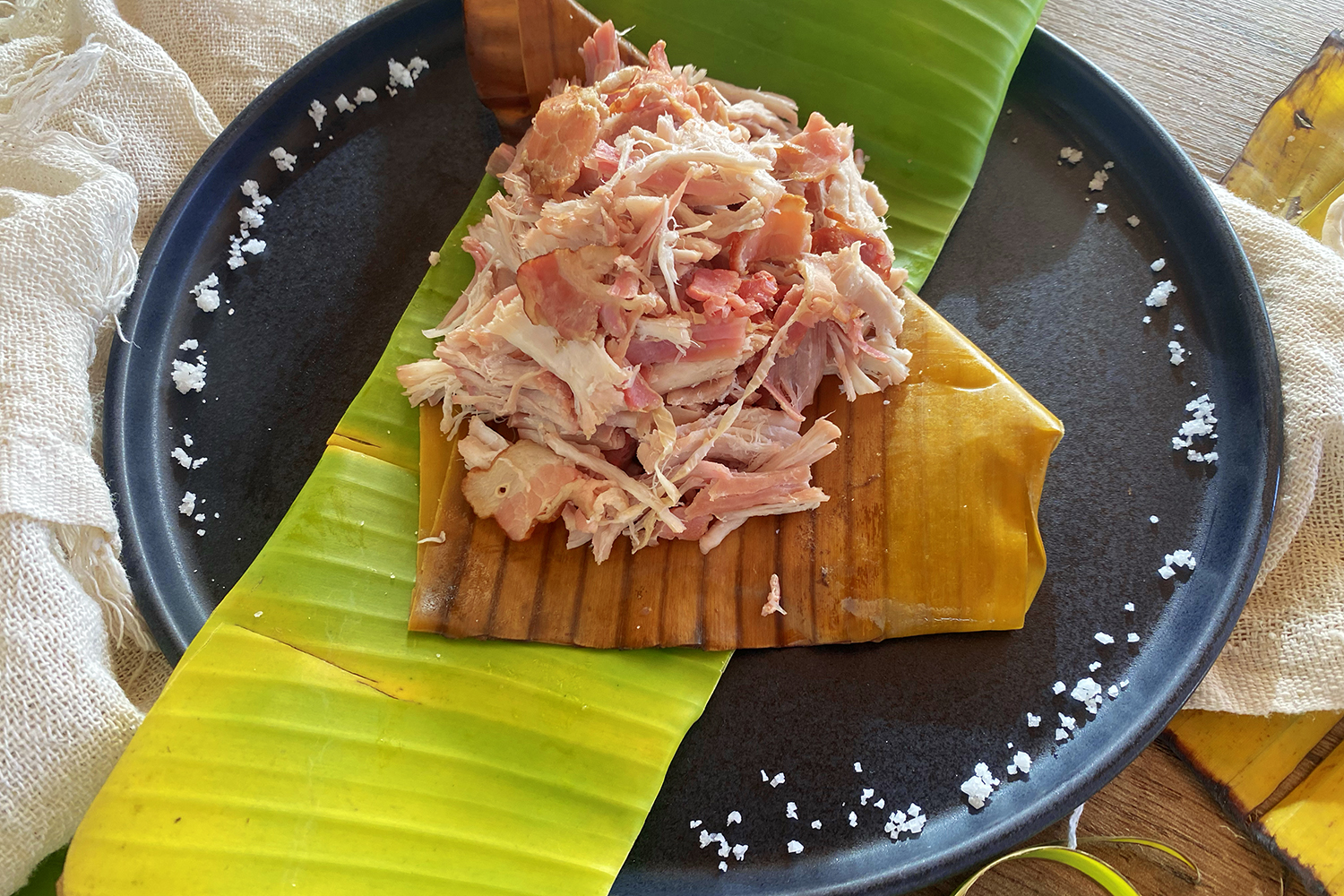 Kalua Pork mixed with bacon on banana leaf on black plate