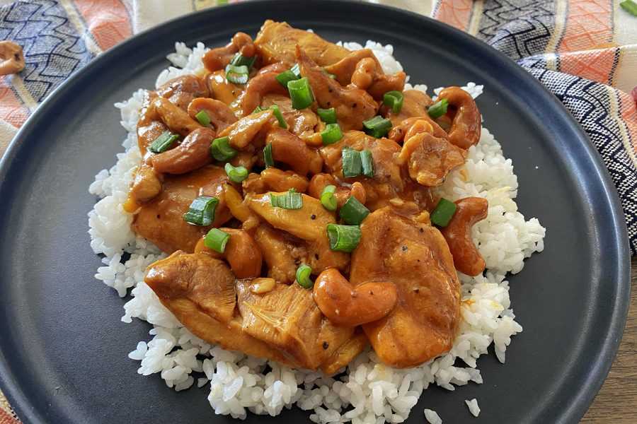 chicken slices and cashew nuts over white rice with spring onion slices on top