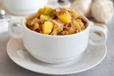 Sausages pieces mixed with potatoes, kale, bacon and spices in white bowl