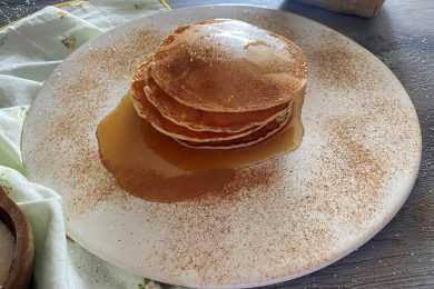 Homemade pancakes laying on each other with maple syrup on top and on the plate