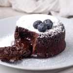 Small chocolate cake with chocolate spilled from the middle topped with blueberries and sugar powder