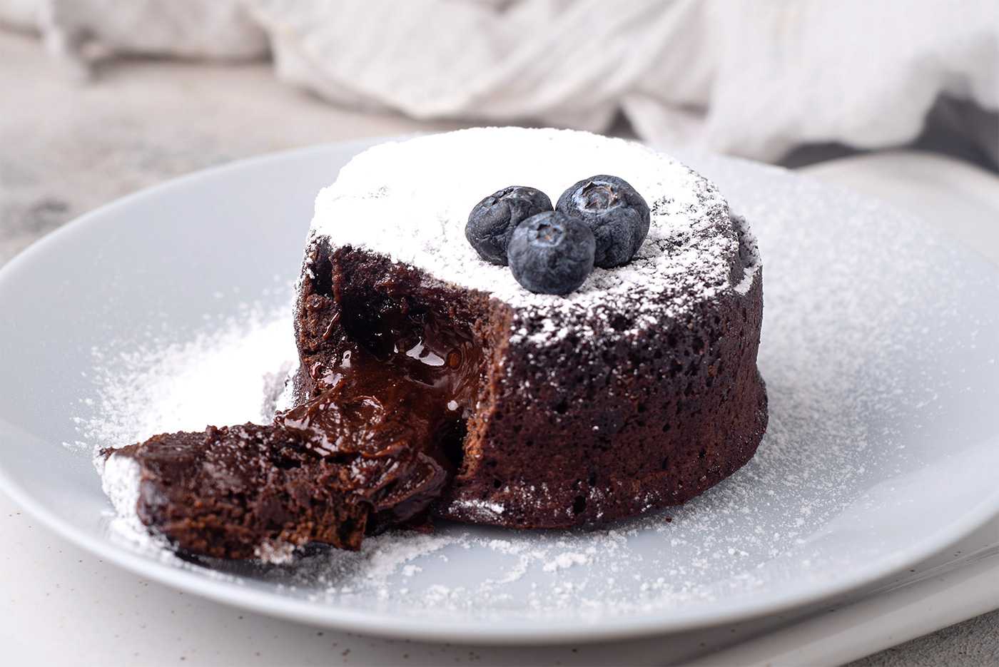 Small chocolate cake with chocolate spilled from the middle topped with blueberries and sugar powder