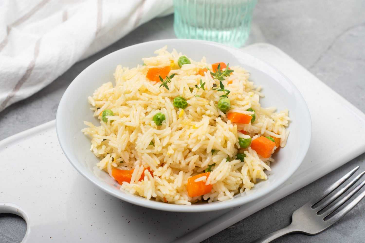 Cooked rice mixed with peas and carrot cubes served in a white plate