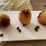 Three baked apples with a sugary frosting on a white plate with raisins on side