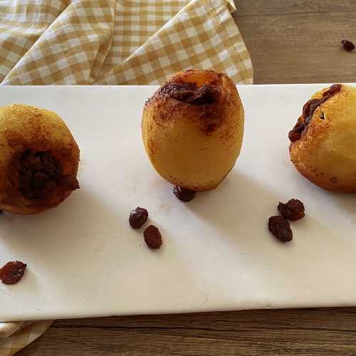 Three baked apples with a sugary frosting on a white plate with raisins on side
