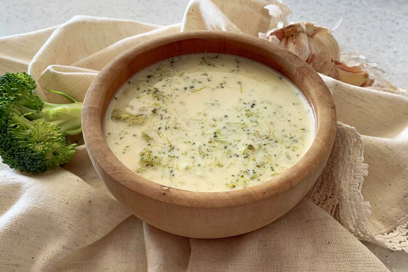Broccoli Cheese Soup inside a brown wooden bowl with a broccoli floret on side