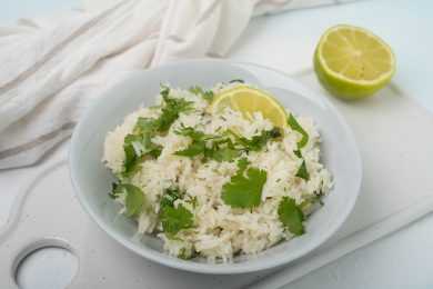 Jasmine rice mixed with chopped cilantro with lime slice on top in white bowl