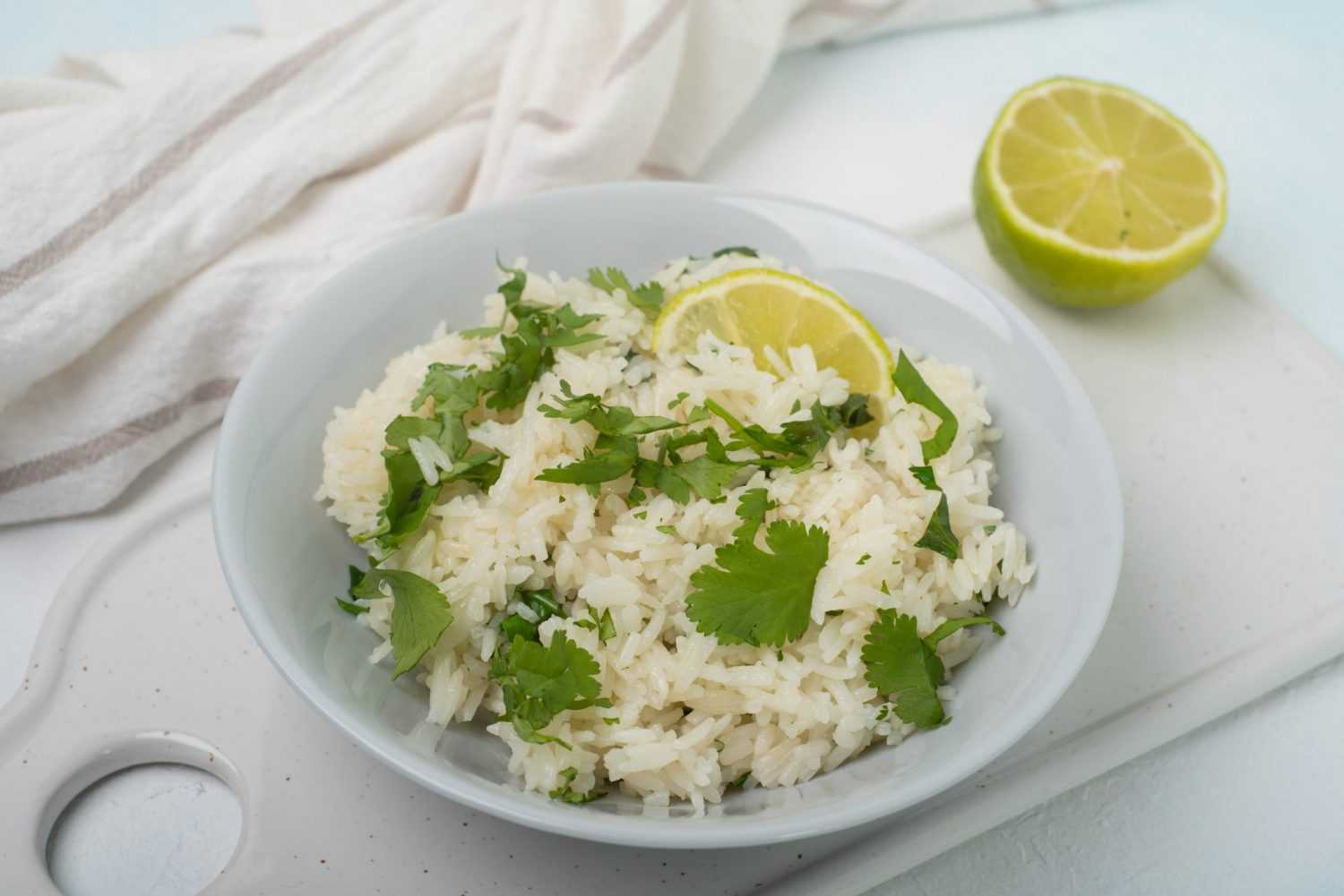 Jasmine rice mixed with chopped cilantro with lime slice on top in white bowl