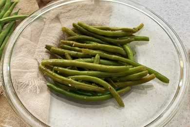 Cooked Green Beans on a transparent plate topped with sesame seeds