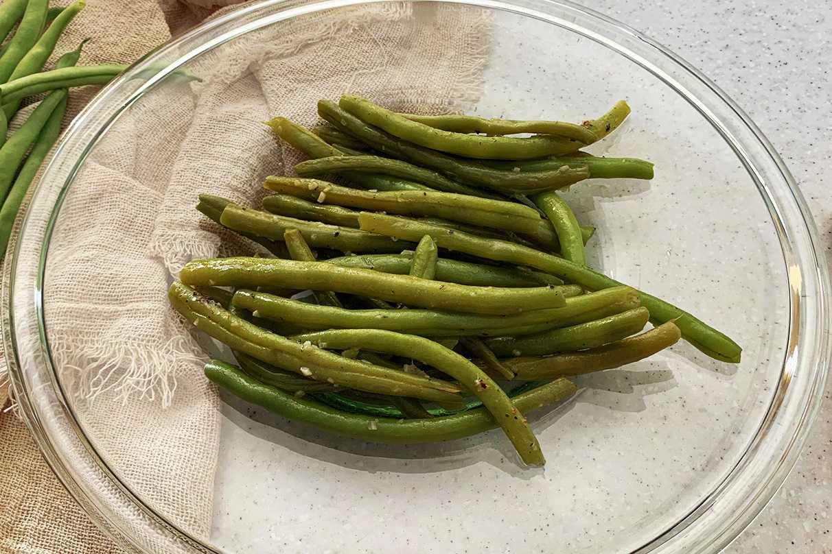 Cooked Green Beans on a clear plate topped with minced garlic
