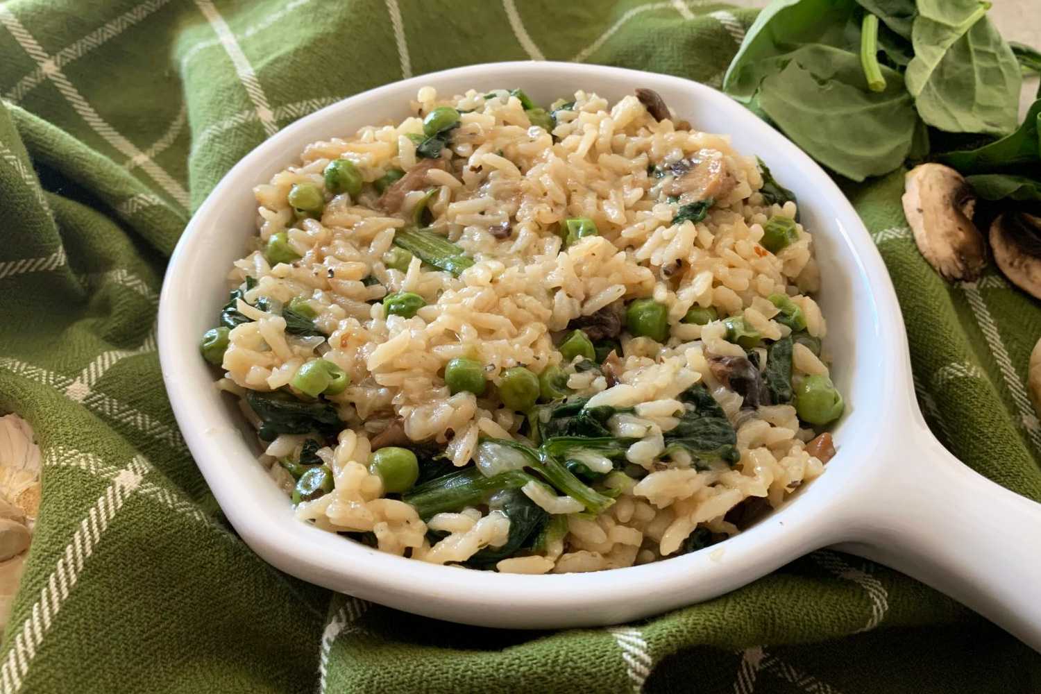 Risotto mixed with peas, sliced ​​mushrooms and spinach in white plate with whole mushrooms and garlic on side