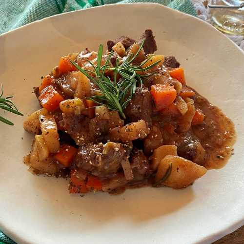 Venison stew cubes with carrot and potato cubes in brown sauce topped with rosemary