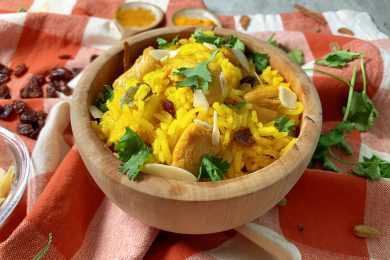 Yellow rice mixed with sliced almonds, parsley and chicken cubes in brown bowl