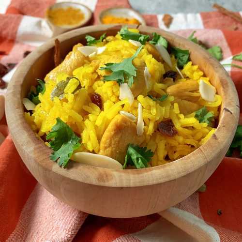 Yellow rice mixed with sliced almonds, parsley and chicken cubes in brown bowl