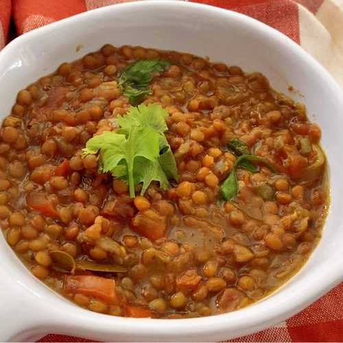 Split lentils mixed with tomatoes, onion and spices in brown sup topped with parsley